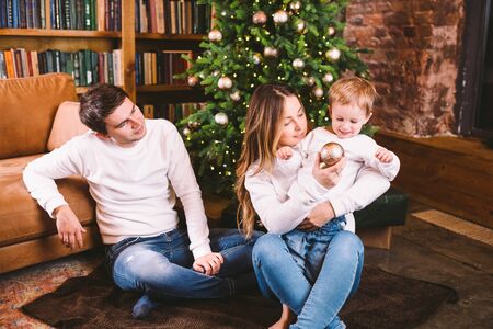 Family Christmas Concept. Lovely family sits near Xmas tree on winter evening.