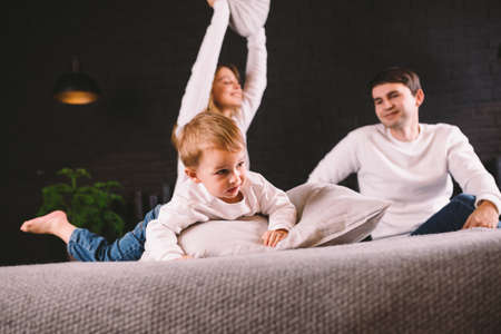 parents with smiling child playing pillow fight on bed, happy family having fun in bedroom, enjoying leisure activity, funny weekend lifestyle. Happy family having fun in bedroom, pillow battle.の写真素材