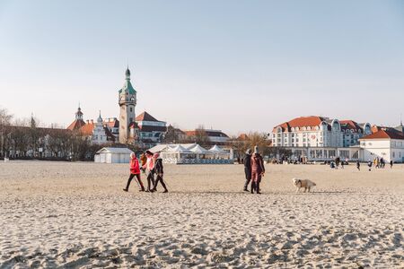 People walk on sandy beach in winter. Perfect winter vacation. People chill out in cold season on coast. Gdansk, Poland February 9, 2020. Walking crowd of people in city Sopot along beach Baltic Sea.のeditorial素材