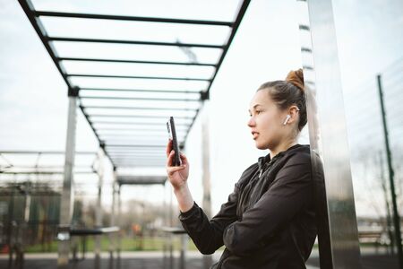 Woman athlete in tattoos, in city, resting after workout fitness, workout. Headphones smartphone....