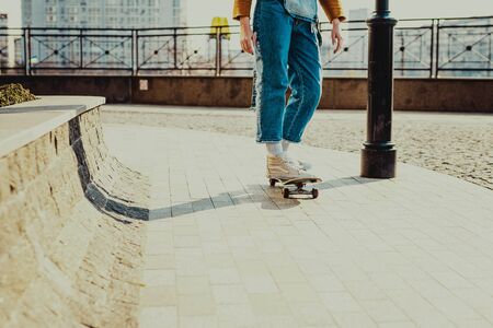 Skateboarding Woman In The City. Skater girl in denim is riding her board on the square. Athletic...