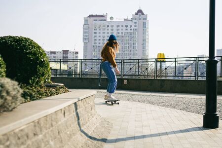 Skateboarding Woman In The City. Skater girl in denim is riding her board on the square. Athletic Woman skateboarder. Building on the background. Concept of leisure activity, urban and sport.の写真素材