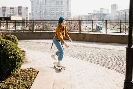 Skateboarding at city. Female, enjoyment. Hipster girl riding skate board. Ride, style. Extreme sport and emotions concept. Alternative lifestyle. Woman skateboarder skateboarding at city.の写真素材