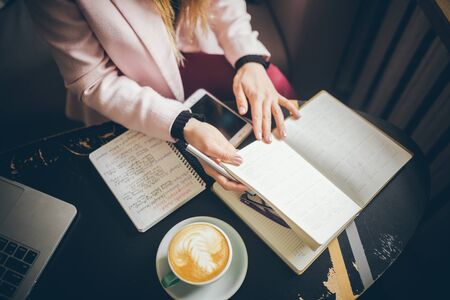 Woman freelancer leafing through pages of a diary in a coffee shop. Entrepreneur working in cafe. Business woman uses paper reminders and schedules. Girl writes notes diary, makes business plan.の写真素材