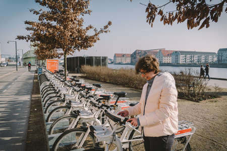 Bike rental service in Copenhagen, Denmark February 18, 2019. Woman taking one bicycle for rent. Ecological transport. Female ready rent bicycle. Tourist taking cycle in bike sharing platform.のeditorial素材