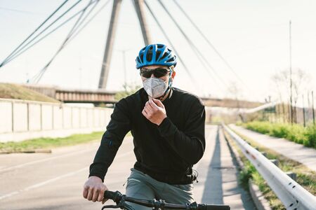 male cyclist on mountain bike in protective mask respirator in polluted city. guy ride to work on environmentally friendly transport, urban eco raffic. Face pollution mask smog dust pm2.5 protection.の写真素材