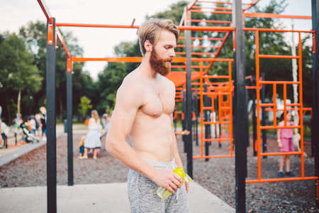 Sporty muscular man drinking water from sport bottle after workout at street gym. Thirsty man...