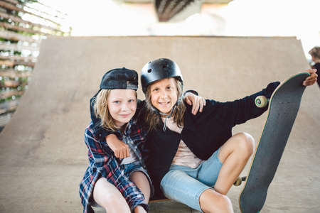 A group of skateboarders children posing on ramp in city skatepark. Friends spend active time riding skateboard in the park. Playground for street sports. Youth, togetherness and friendship concept.の写真素材