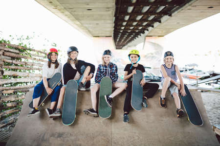 Happy friends in city park for extreme sports. Little ones having fun on skating ramp outdoor . Youth and friendship. Caucasian riders having fun together on sports urban area for skateboarding.の写真素材