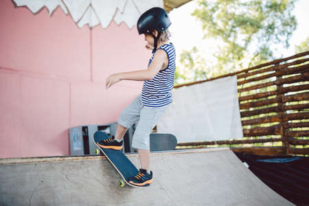 Caucasian boy in a helmet does tricks on a skateboard on a playground for skateboarding outside. A child skateboarder rides a halfpipe ramp at a skatepark. Extreme sport and children.の写真素材