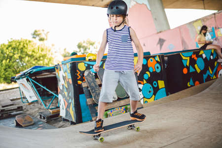 Skater boy rides on skateboard at skate park ramp. Kid practising skateboarding outdoors on skatepark. Youth culture of leisure and sports. Skateboarder doing trick on skateboard on halfpipe ramp.の写真素材