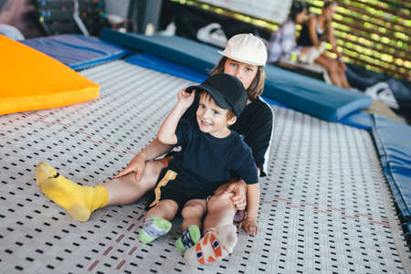 Two happy emotions children, brothers playing and having fun while jumping on bouncing trampoline in playground in summer. Hug, friendship and childhood concept. Active lifestyle of children.の写真素材