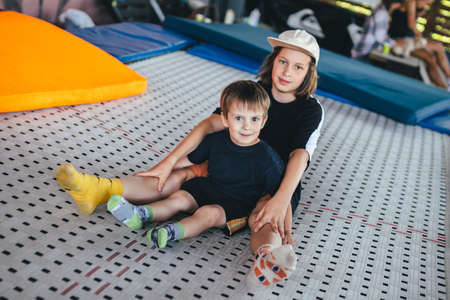 Two Caucasian brothers boys enjoy sitting on a trampoline in an embrace. Children playing together on a trampoline in a sports center. Outdoor gym acrobatics and trampoline. Lets play.の写真素材