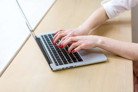 Caucasian red haired woman working at laptop in office at table in front of window. Business woman is typing on computer keyboard. Female employee consult client online, leadership concept.の写真素材