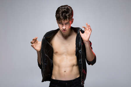 Handsome caucasian guy model with naked tors, lack leather jacket posing in studio on red...