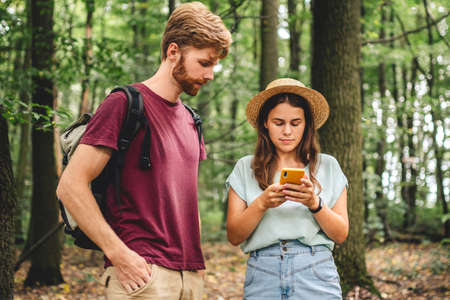 Couple hiking and using maps app on cell phone. Two people hikers looking at mobile phone trying...