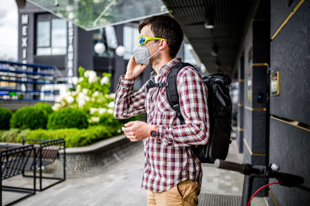 Male courier wearing protective face mask arrived at delivery address on electric scooter. Subject delivery during covid 19 on environmentally friendly transport. Pollution in big city. PM 2.5 mask.の写真素材