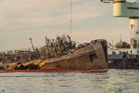 Rescue wrecked oil tanker Delfi in Odessa, Ukraine 26 August 2020, near Black Sea coast. Marine Crane lift wreck Delphi into sea. Old rusty ship lie on side aground, tug pulls ship out after accident.のeditorial素材