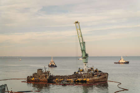 Rescue wrecked oil tanker Delfi in Odessa, Ukraine 26 August 2020, near Black Sea coast. Marine Crane lift wreck Delphi into sea. Old rusty ship lie on side aground, tug pulls ship out after accident.のeditorial素材