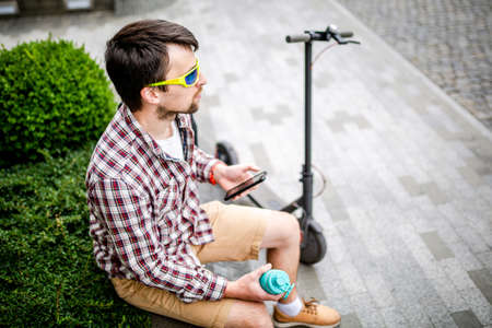 Individual urban environmental friendly transport electric kick scooter parked near man sitting on...