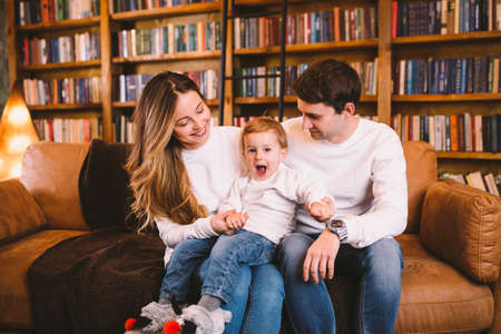 Christmas family portrait. Young Caucasian family in identical clothes having fun on sofa in living...