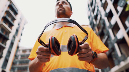 Builder covers his ears, ear muff to protect workers ears. Construction worker wearing protective ear defenders. Concept of construction, taking care of safety during work. Protection against injury.の写真素材