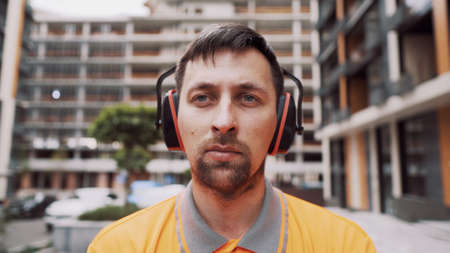 Construction worker with ear muff working at construction site. Worker puts on ear defenders to...