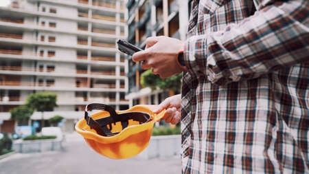 Young Engineer using smartphone on construction site. Architect using phone. Manager development building texting on smart phone. Builder makes notes in application during inspection and verification.の写真素材