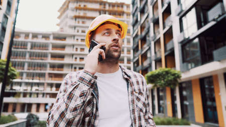 Portrait of young handyman making call while standing at construction area. Engineer talking on the...
