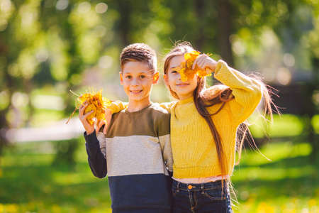 Friendship between siblings. Siblings together outside with bright colored background. Kids autumn portrait. Brother and sister playing in autumn park leaves. Family active fall weekend concept.の写真素材
