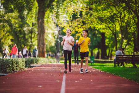 Couple of kids boy and girl doing cardio workout, jogging in park on jogging track red. Cute twins...