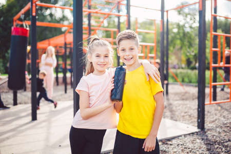 Sportive friends. Brother and sister standing together at street city gym. Children athletes hug smile during workout training. Twins boy and girl posing on playground. Physical development education.の写真素材