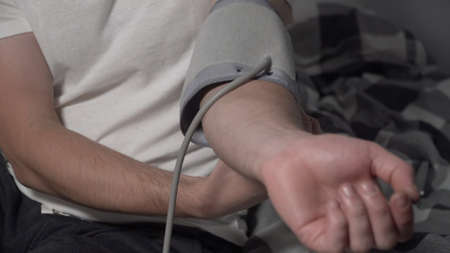Young man measuring blood pressure at home. Hypertensive patient performing an automatic blood...