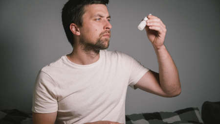 Young Caucasian man holds nasal spray for rhinitis and allergies in his hands and studies composition and instructions for use. Medication or drugs abuse, healthcare concept. Sprays nose with drops.の写真素材