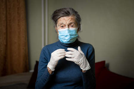 Portrait elderly woman took security measures, wearing gloves and medical mask, ahead of visit by social welfare workers during coronavirus quarantine. Lockdown and loneliness, need for care.の写真素材