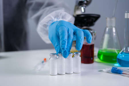 Development and search for drug for coronavirus. Chemist examining ampoule of powdered antibiotic...