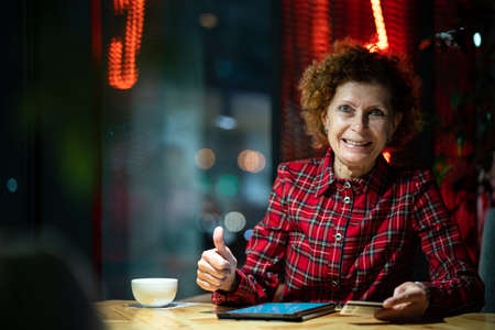 Senior woman shopping online at Christmas sitting in the evening in a cafe shop by the window...