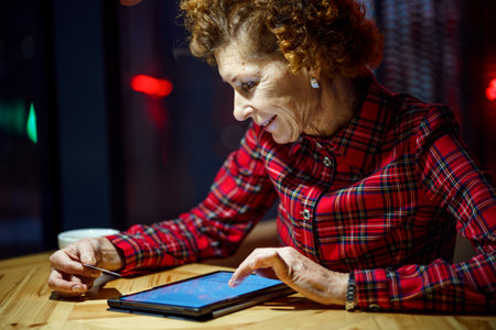 Mature woman makes online purchases using tablet computer in cafe. Older female pays for online payment with credit card. Modern senior uses plastic cards for online shopping. Banking online.の写真素材