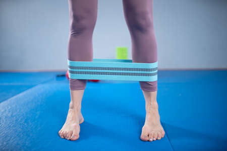 Athletic woman in sportswear barefoot using thick elastic fabric workout bands for stretch fitness...