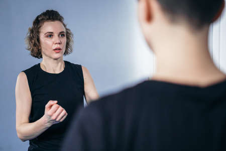 Young woman karate student with her trainer in gym. Taekwondo coach teaching adult woman in personal...