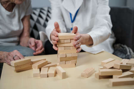 Dementia therapy in playful way, training fingers and fine motor skills, build wooden blocks into tower. Senior woman 90 years old and doctor playing educational game in nursing home.の写真素材