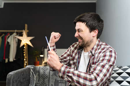 Young caucasian man holding pregnancy test in his hands very excited and happy with result and...