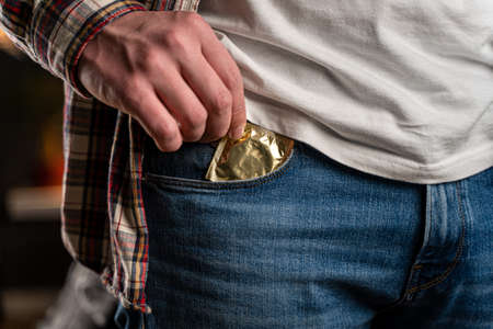 Caucasian man hand close-up takes out condom in gold package from jeans pocket. Sex theme with protection. Safe sex. Prevention of sexually transmitted diseases, infections, aids. Healthcare.の写真素材