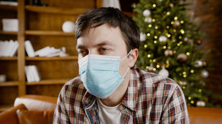 Depressed man in medical mask at home on the couch for Christmas.の写真素材