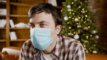 Depressed man in medical mask at home on the couch for Christmas.の写真素材