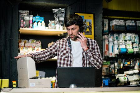 Man takes order by phone in his sporting goods store for sports and tourism sitting at table near computer talking on smartphone. Theme is small business. Sales clerk on phone in bike shop.の写真素材