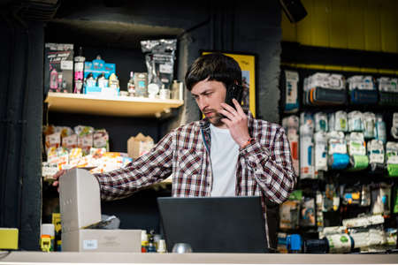 Bike shop owner at work. Store employee takes an order by mobile phone at table near laptop in travel and sporting goods store. Small business, communication, people and service concept.の写真素材