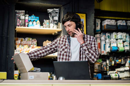 Man takes order by phone in his sporting goods store for sports and tourism sitting at table near computer talking on smartphone. Theme is small business. Sales clerk on phone in bike shop.の写真素材