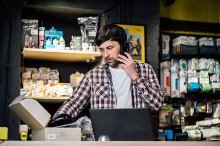 Small business owner on phone and computer in store. Sport shop worker making call with cell phone. Salesman working and talking on cell phone in bicycle shop. Seller taking orders by phone.の写真素材