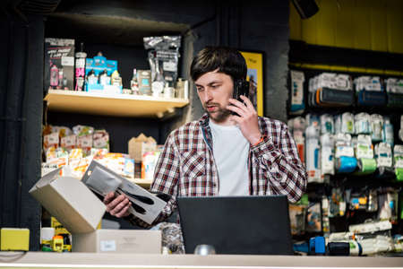 Small business owner on phone and computer in store. Sport shop worker making call with cell phone. Salesman working and talking on cell phone in bicycle shop. Seller taking orders by phone.の写真素材